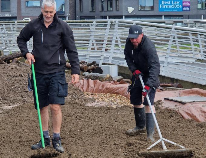 Two of The Deep's Aquarist team helping rake mud into the bog garden.